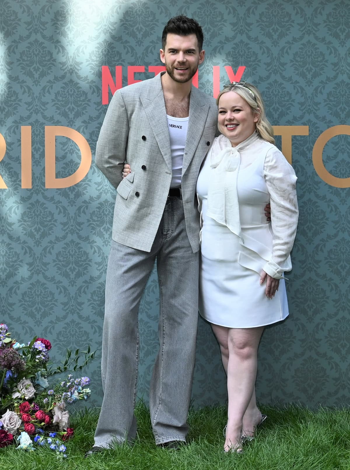 Height Contrast at Bridgerton Photocall: Luke Newton towers over Nicola Coughlan, highlighting their striking height difference as they pose together in stylish Versace outfits