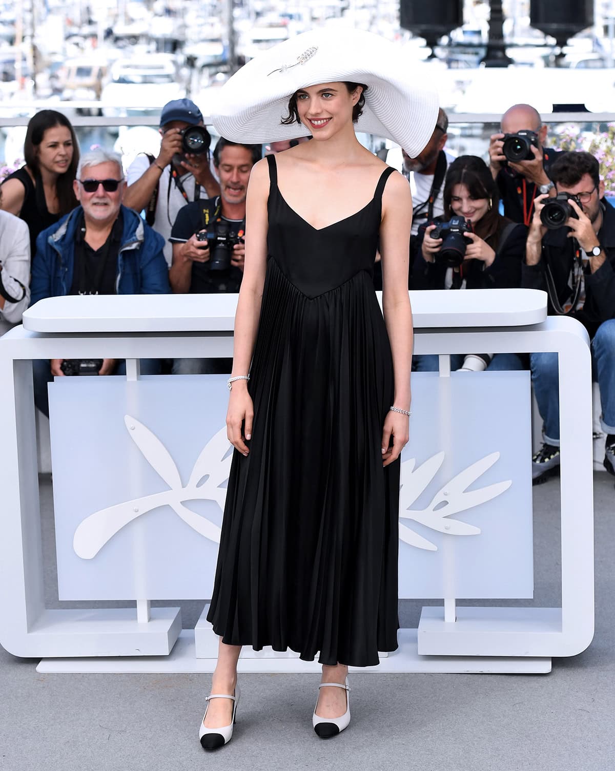 Margaret Qualley embraces 1980s summer French chic in a flowy black plunging dress by Chanel with an oversized white hat on the French Riviera