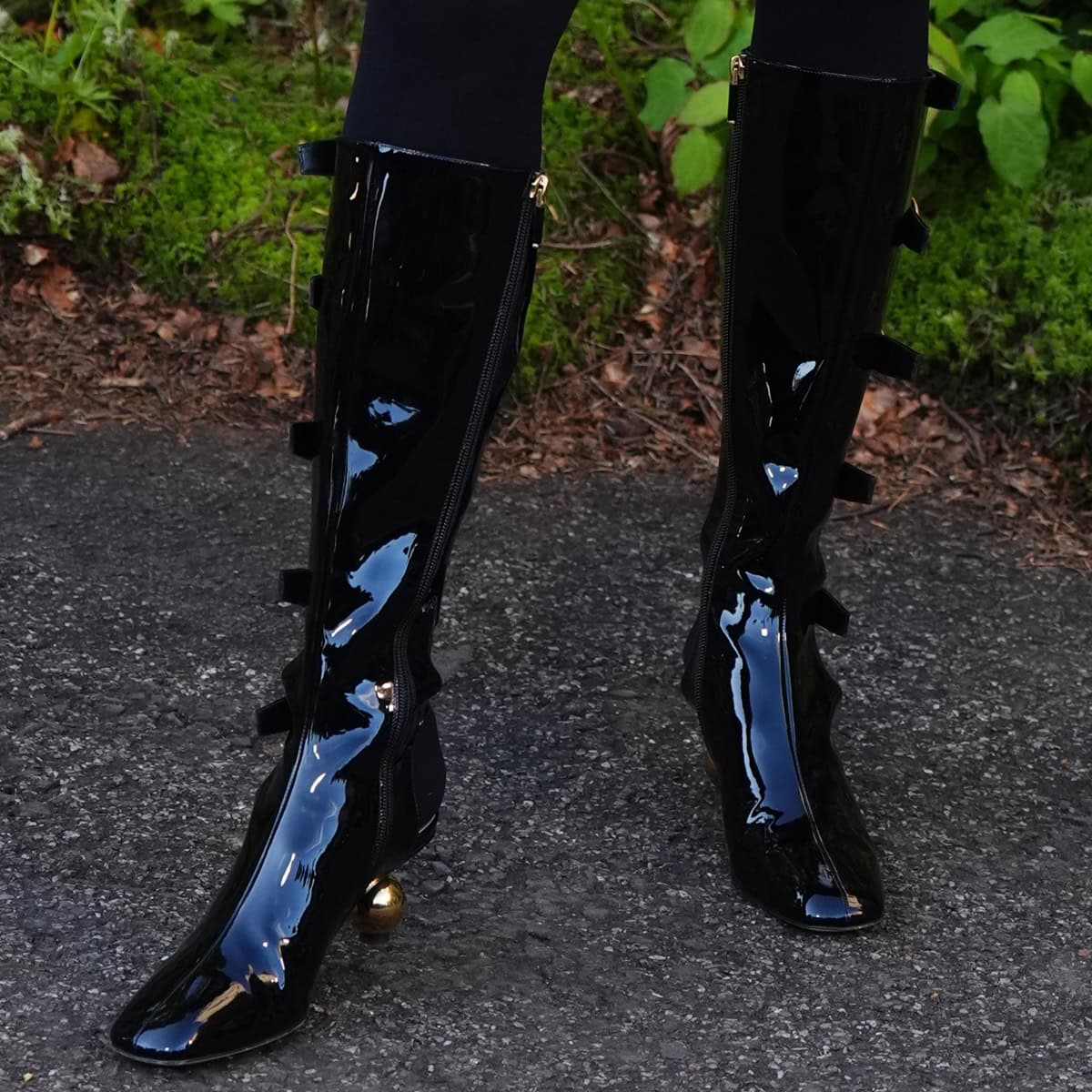 Anya Taylor-Joy's black patent leather boots feature a sleek high-gloss finish, square toes, multiple buckles on the shaft, and a side zipper for easy wear