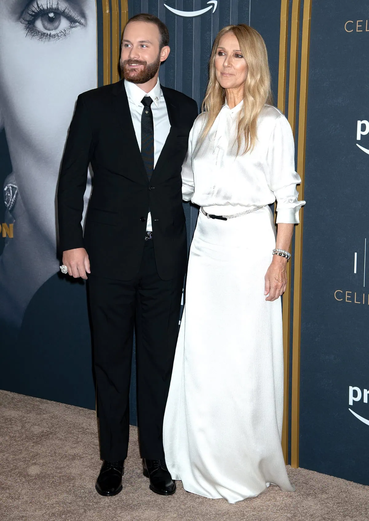 Celine Dion wears a white Dior pussy-bow blouse with a white maxi flared skirt and a crystal belt as she poses with her eldest son, René-Charles Angelil, who looks handsome in a classic black suit