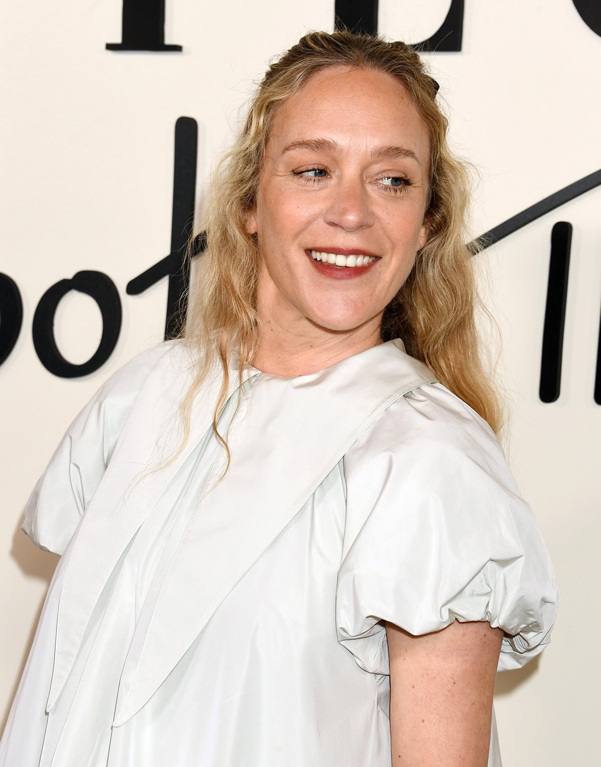 Chloe Sevigny adds a coquette element to her whimsical look by styling her long curly tresses with a black bow