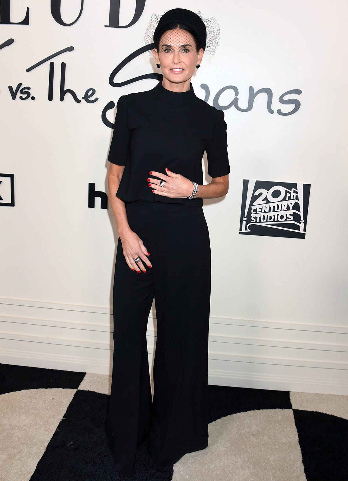 Demi Moore channels retro glamour in an all-black Carolina Herrera ensemble featuring a wool-blend mock-neck tee and flared pants