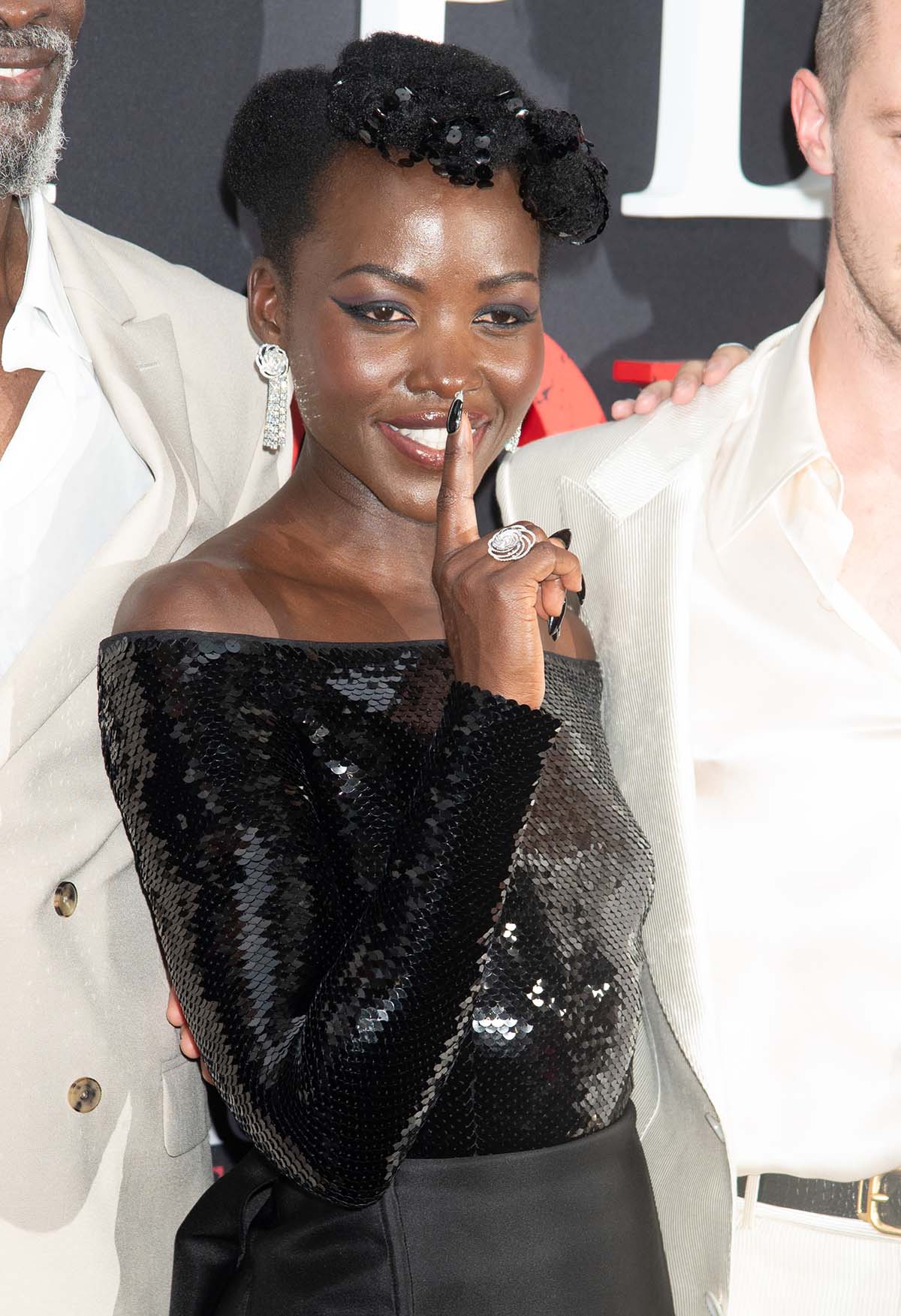 Lupita Nyong'o fashions her pixie hair with sequin-adorned afro bangs and wears cat eye makeup to enhance the ensemble's feline theme