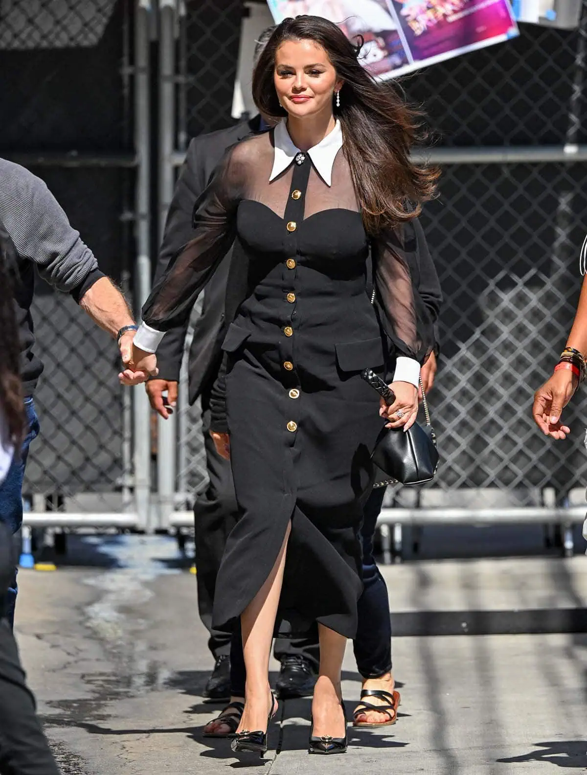 Selena Gomez exudes elegance in a black Versace dress with sheer sleeves and panel, gold Medusa buttons, a white Swallowtail collar, and white cuffs
