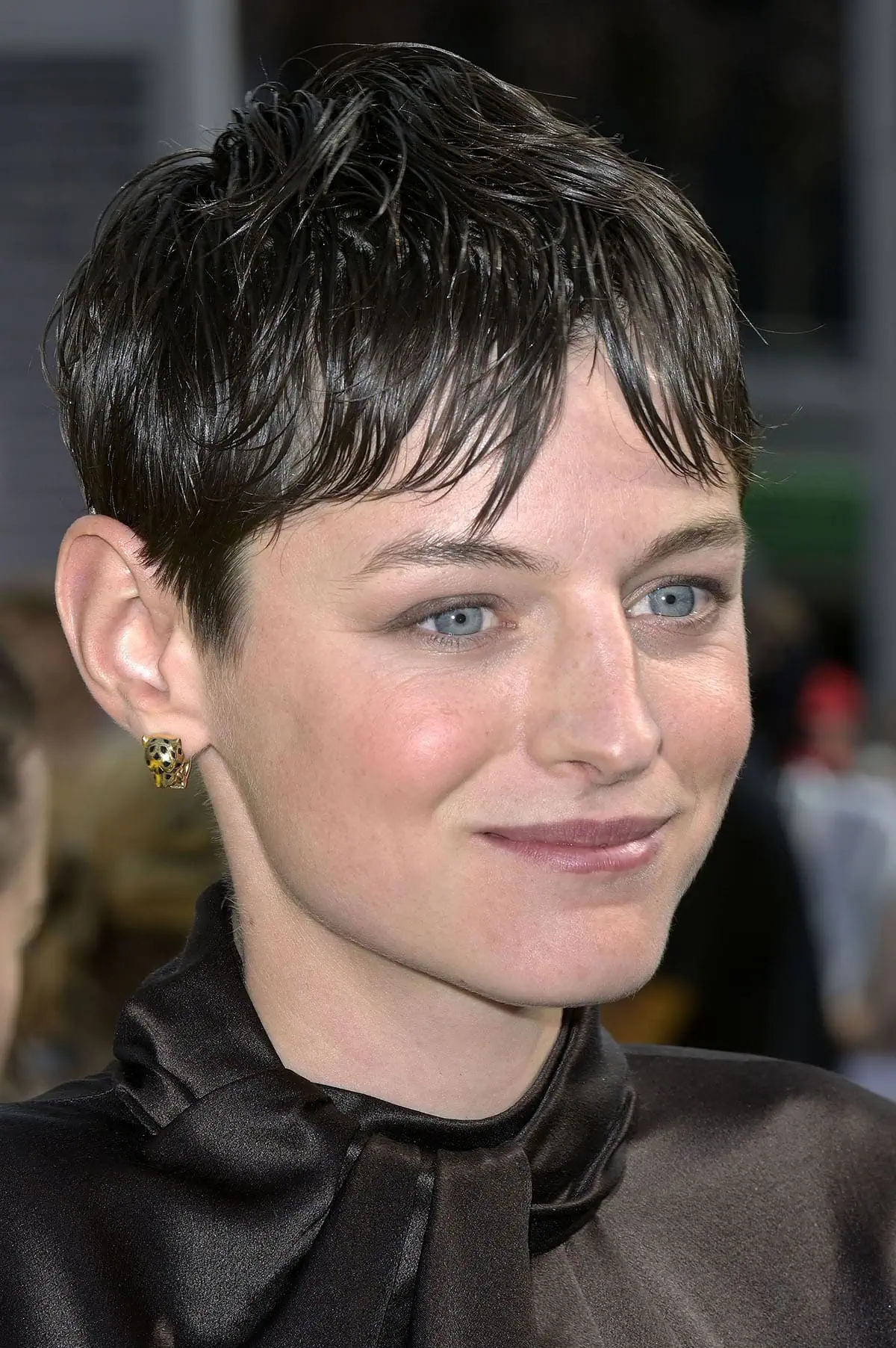 Emma Corrin mirrors their supervillain persona by arranging their pixie hair in a messy, wet-look style and sporting minimal makeup