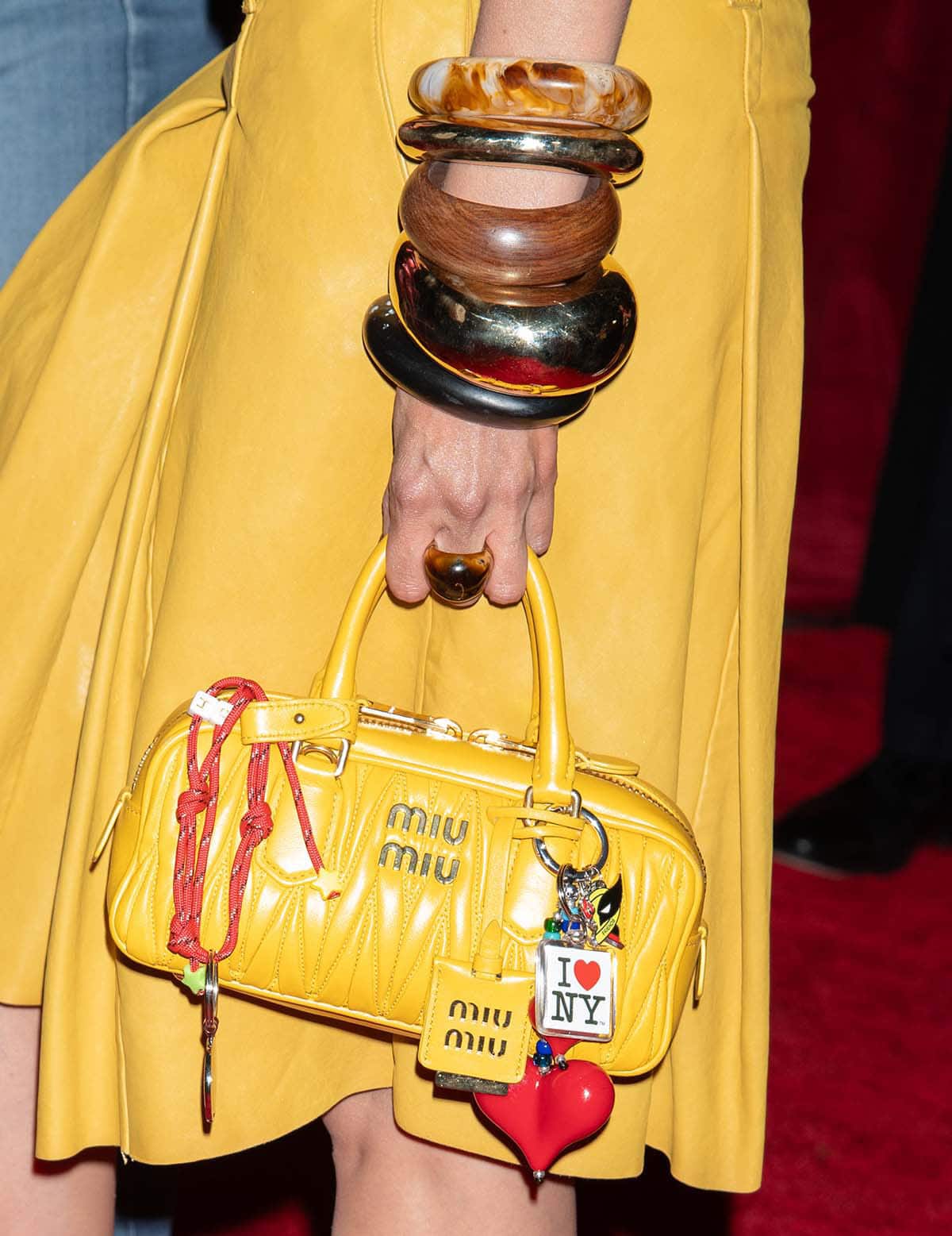 Gigi Hadid carries a yellow Miu Miu bag adorned with Deadpool and Wolverine charms and styles her look with chunky bangles from Alexis Bittar and Dinosaur Designs