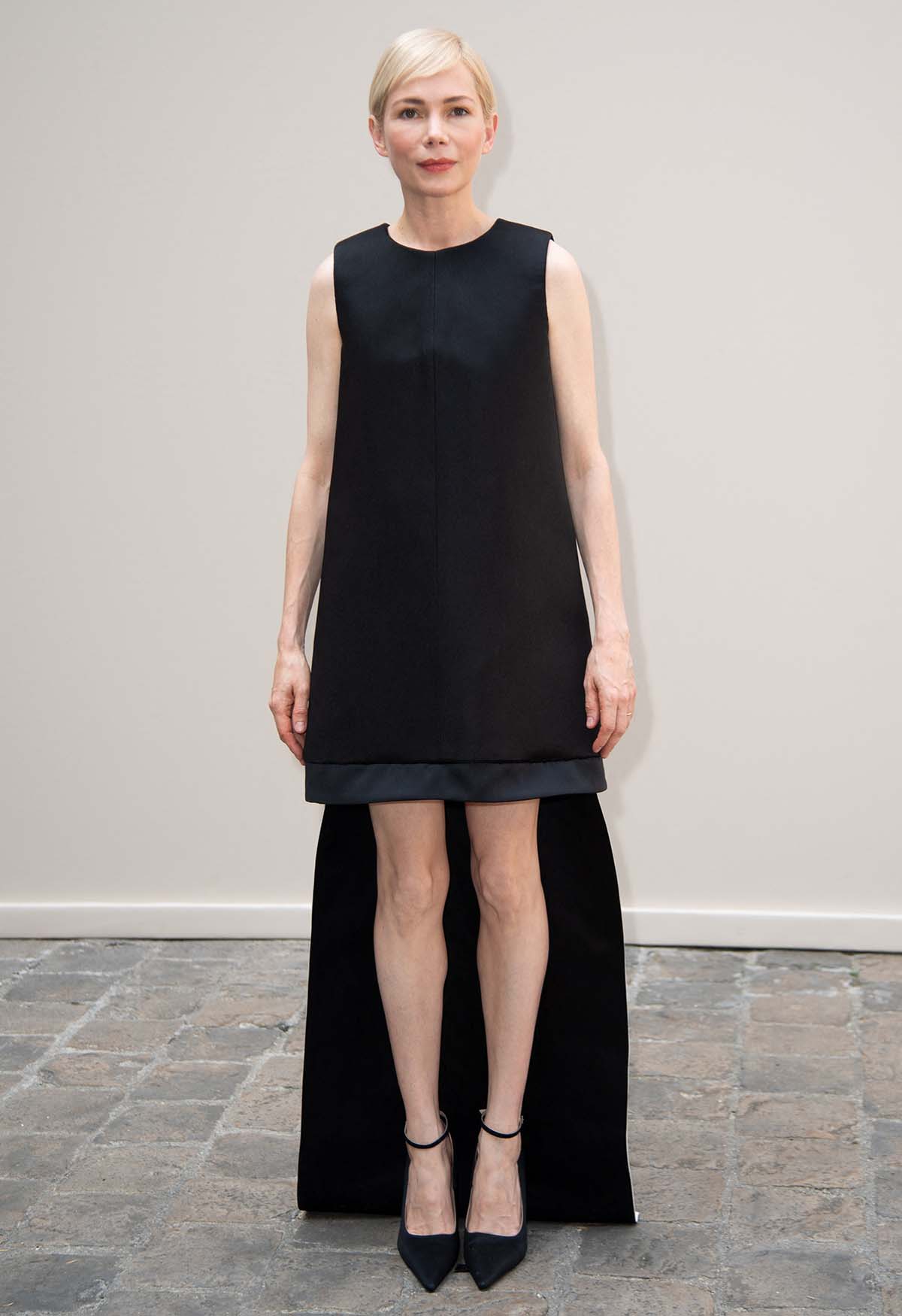 Michelle Williams opts for understated elegance in a black Ashi sleeveless shift dress with a high-low hem, allowing her to showcase her legs, at the Ashi Studio Paris Fashion Week Haute Couture Fall/Winter 2024-2025 show