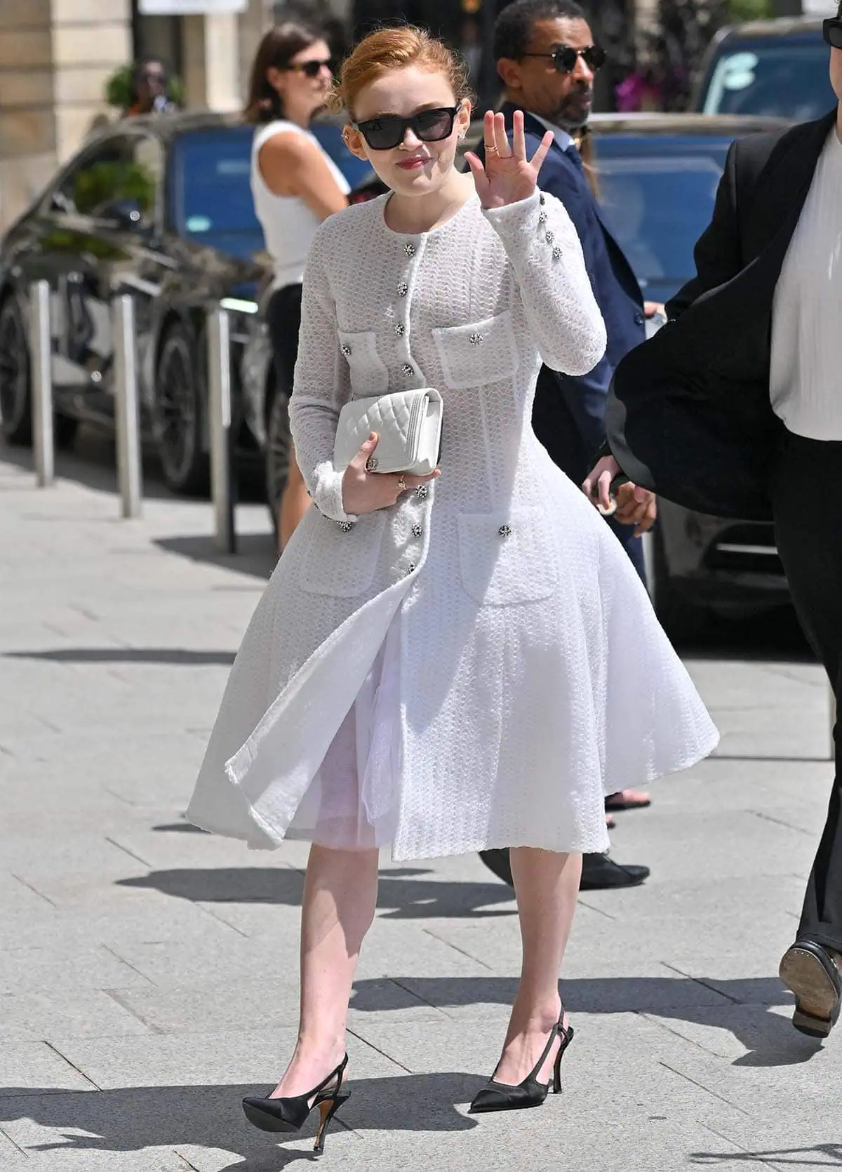 Sadie Sink exudes elegance in a white Chanel A-line dress featuring a fitted long-sleeved bodice and a structured skirt with a petticoat at Chanel's Paris Fashion Week presentation