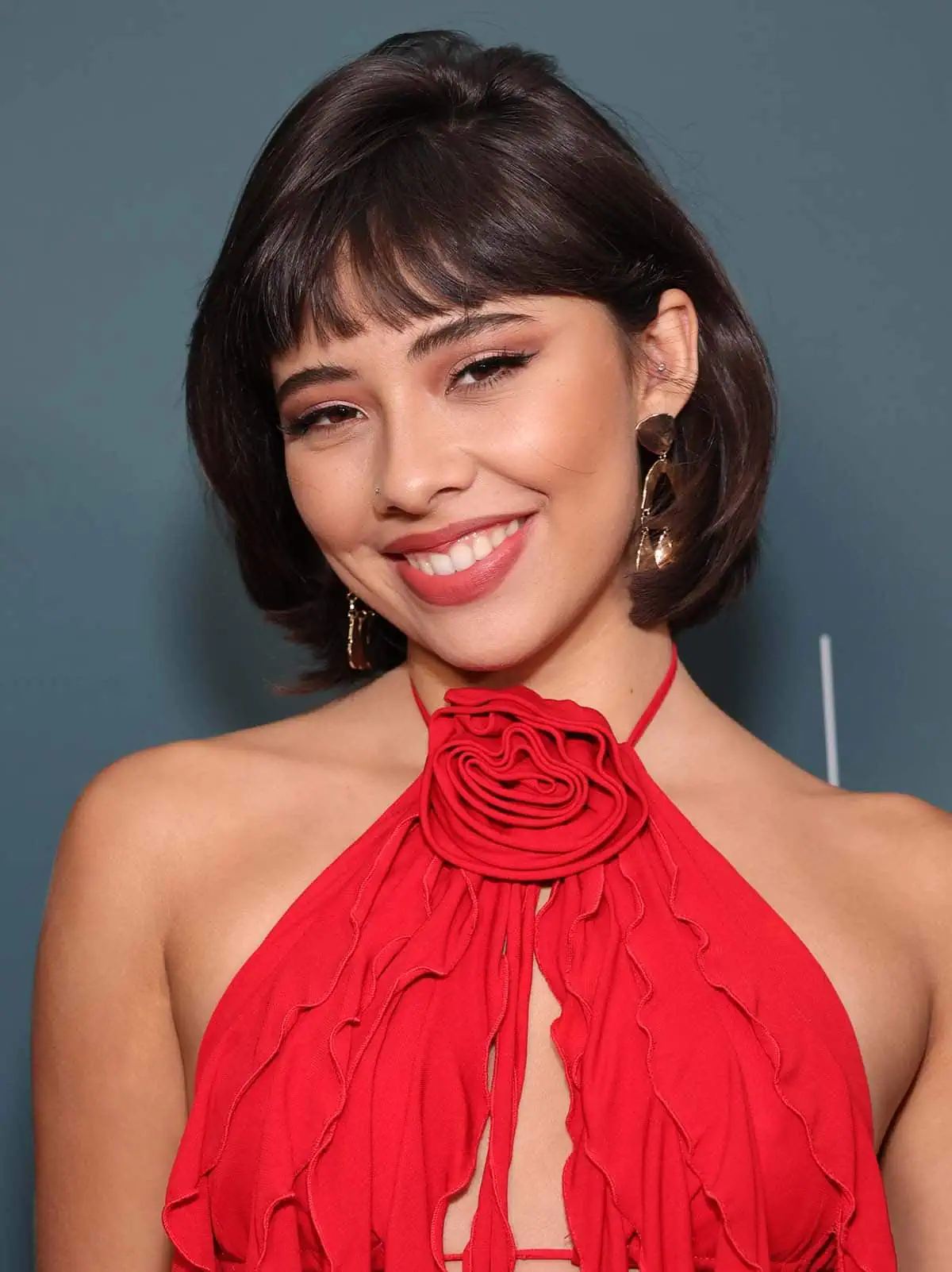 Xochitl Gomez wears coordinating reddish-brown makeup with a retro-style bouffant bob and her signature blunt bangs