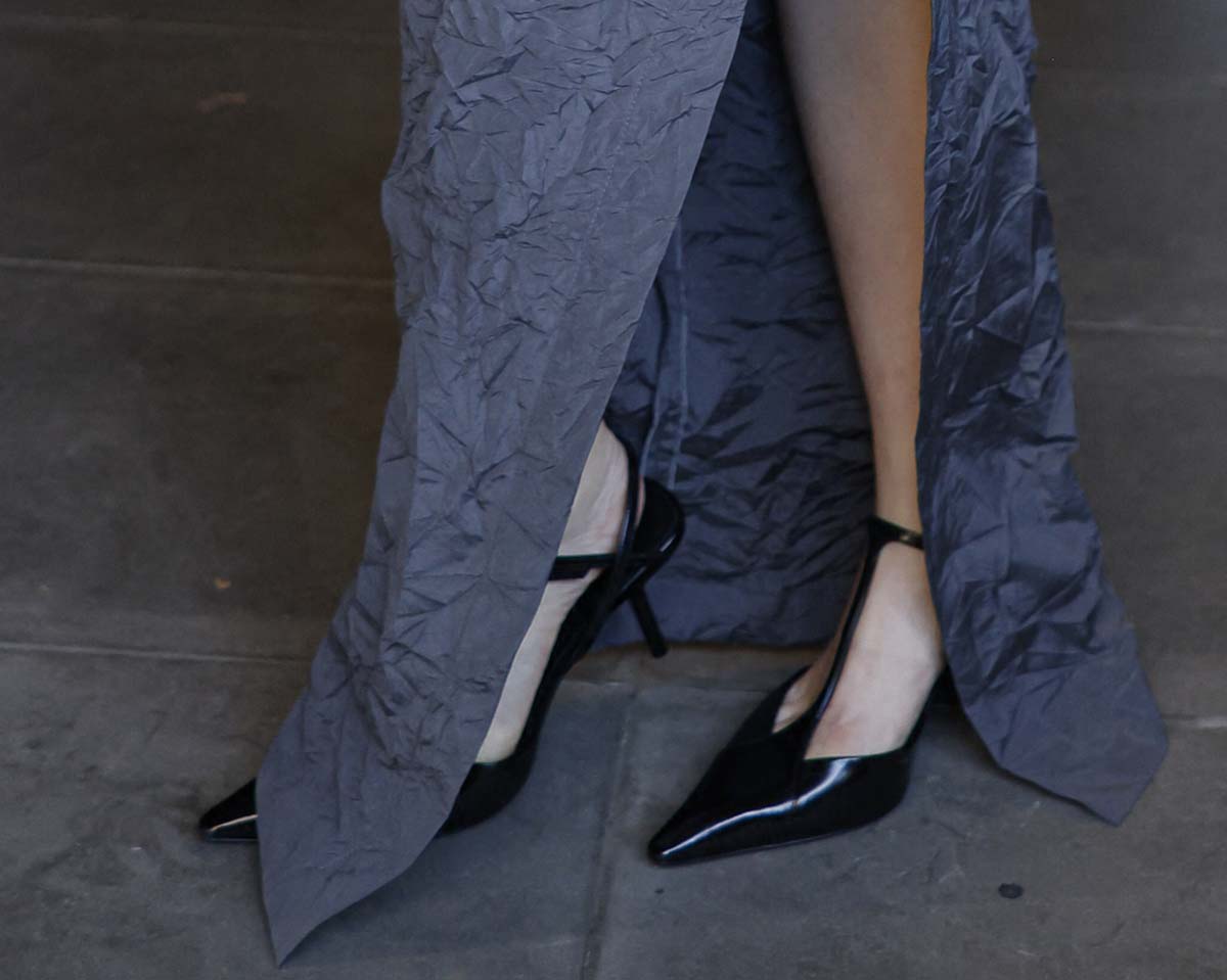 Joey King teams her gray collared ruched maxi dress with pointy black pumps featuring slim T-straps and pin heels