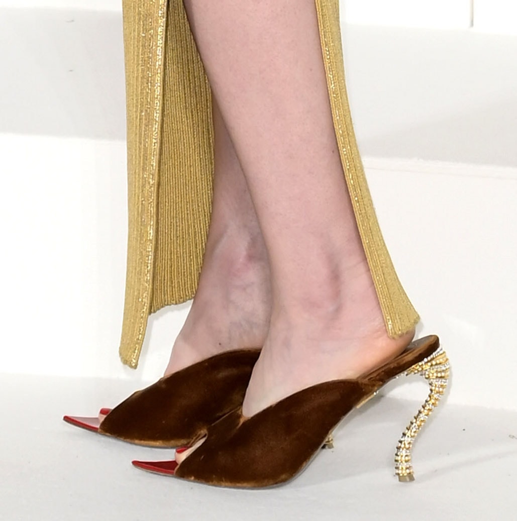 Lily Collins pairs her golden dress with the whimsical Bijoux mules by Schiaparelli featuring S-shaped bejeweled heels