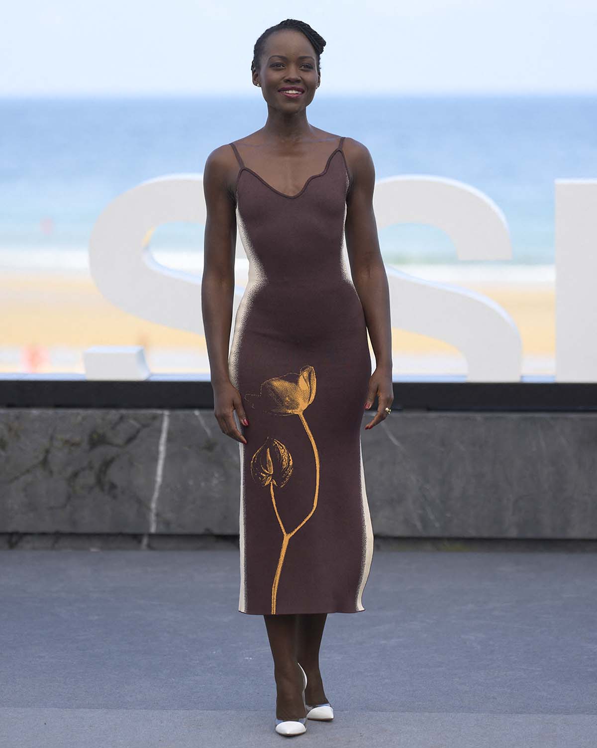 Lupita Nyong'o looks chic in a brown tank slip dress by PH5 featuring a digitally coded artificial flower print and white airbrushing along the sides, creating an hourglass illusion