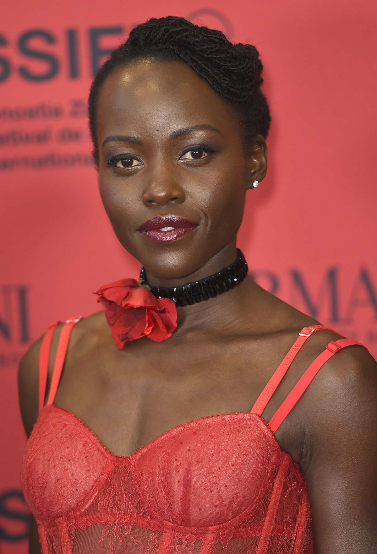 Lupita Nyong'o styles her flamenco red dress with a red floral choker and fashions her sister locs in a bun