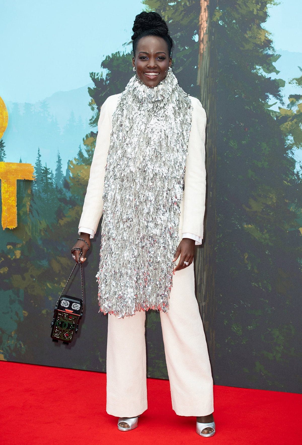 Lupita Nyong'o looks Christmassy in a Chanel tweed suit with an eccentric silver tassel scarf