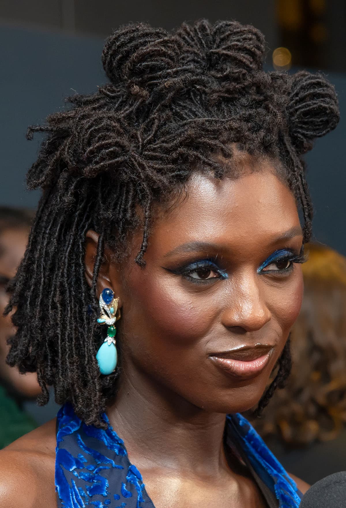 Jodie Turner-Smith accessorizes her electric blue dress with David Webb jewels, wears metallic blue eyeshadow, and styles her braided hair in a crown of four top knots