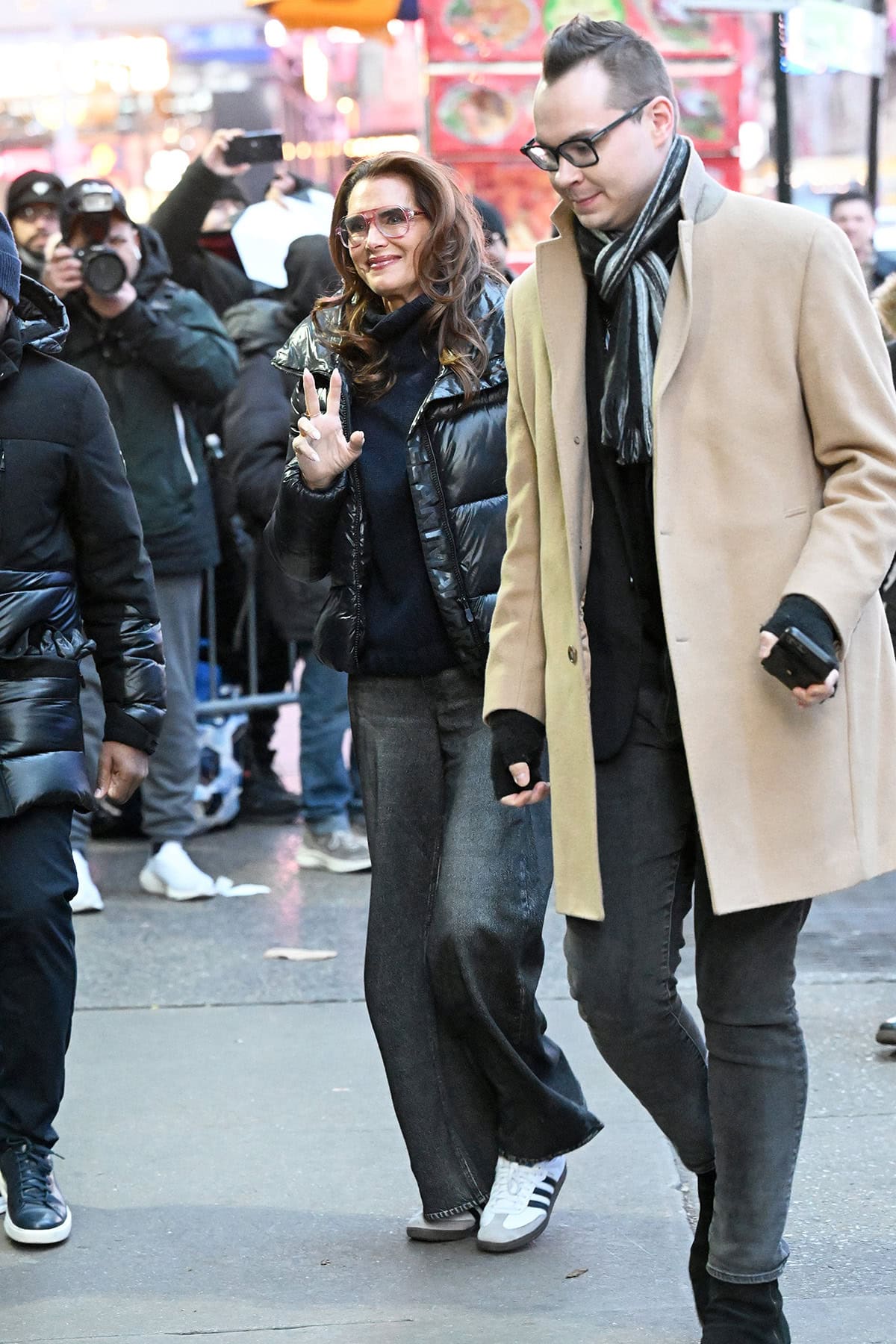 Brooke Shields bundles up in a black sweater, a black puffer winter jacket, jeans, and Adidas Samba sneakers