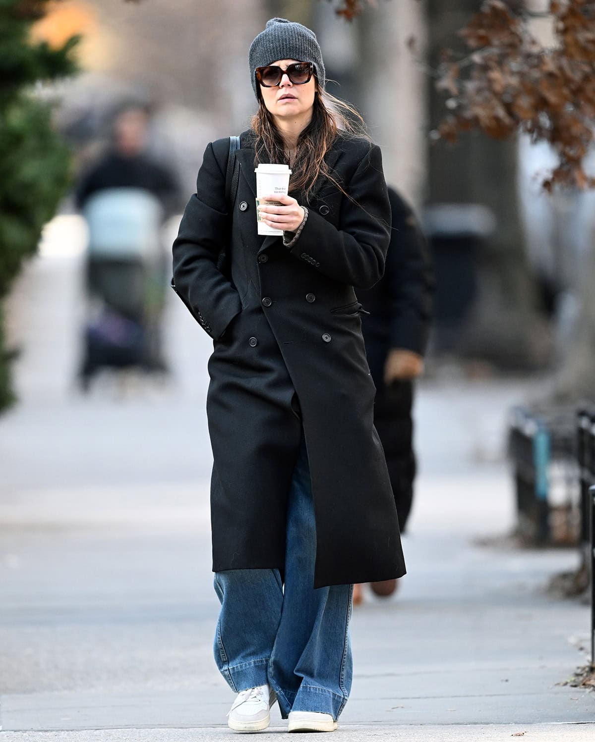 Katie Holmes opts for her go-to winter outfit formula, wearing a black coat with baggy jeans and white sneakers