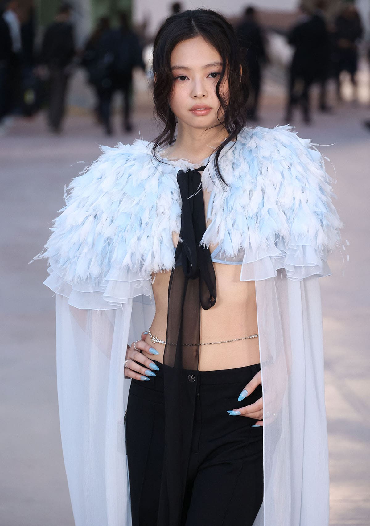 Jennie Kim turns heads in her midriff-baring Chanel outfit featuring a sheer blue bra top, a feathered cape, and a pair of black trousers