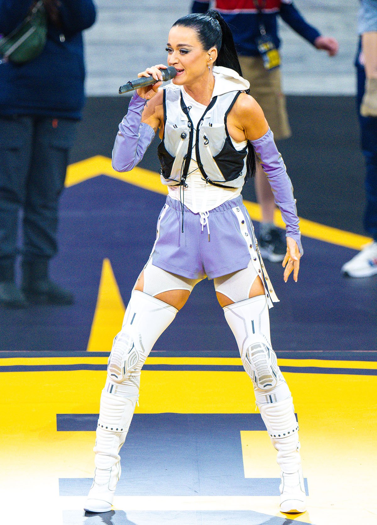 Katy Perry teams her Vetements x New Rock knee-high biker boots with color-changing shorts, white leggings, a white corset, and Salomon’s ADV Skin Cross Seasons Race Flag running pack