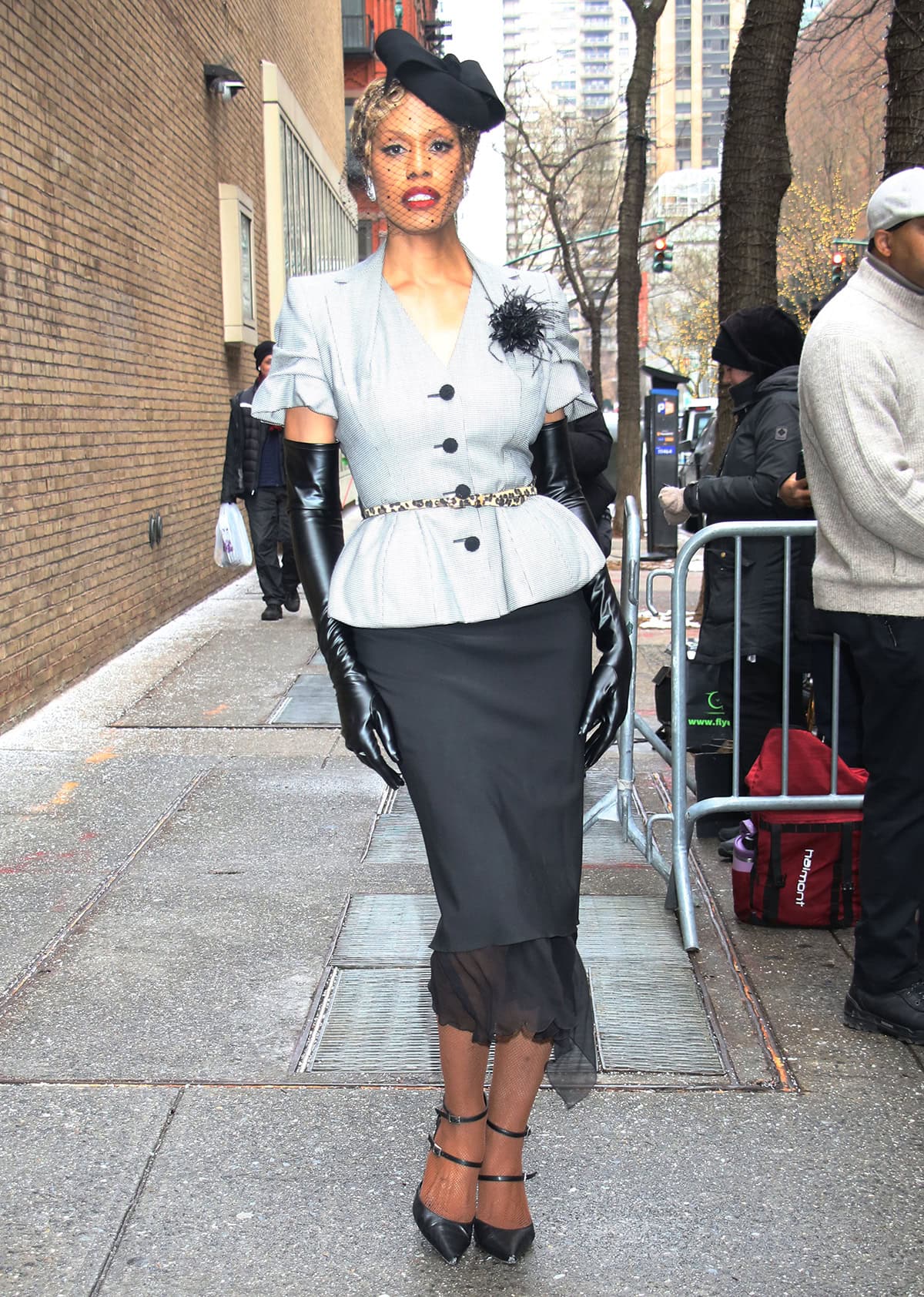 Laverne Cox embraces retro fashion, wearing a gray John Galliano blazer with ruched sleeves and a black pencil skirt with sheer trims evocative of Madonna's iconic outfit from her 1994 Take a Bow music video