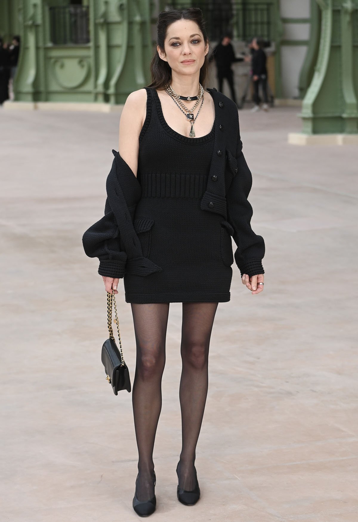 Marion Cotillard puts a rebellious grunge twist on Chanel's black sleeveless knit mini-dress, styling it with a black cardigan and layers of black and gold chain necklaces