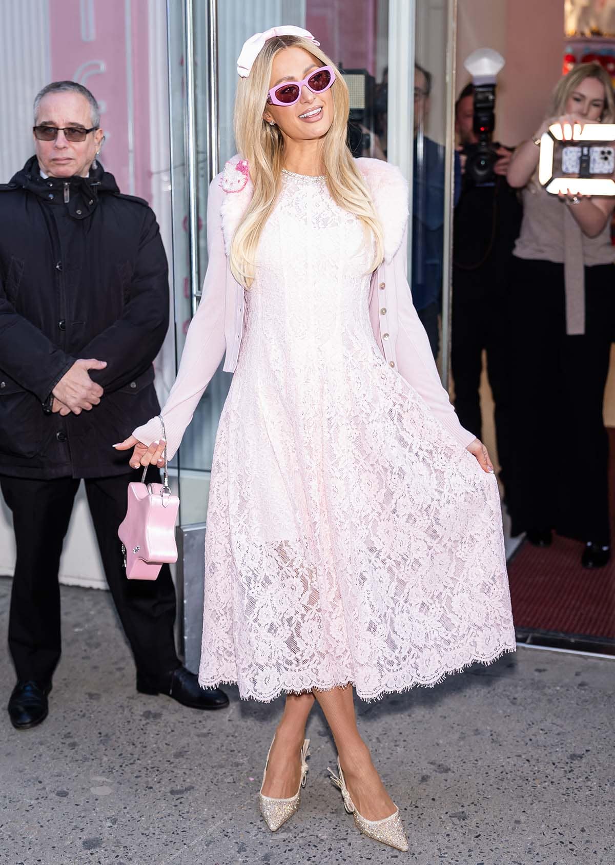 Paris Hilton looks too twee and feminine in a pink lace Self-Portrait dress, a pink cardigan with a furry collar and a Hello Kitty accent, pink sunglasses, and a pink head bow