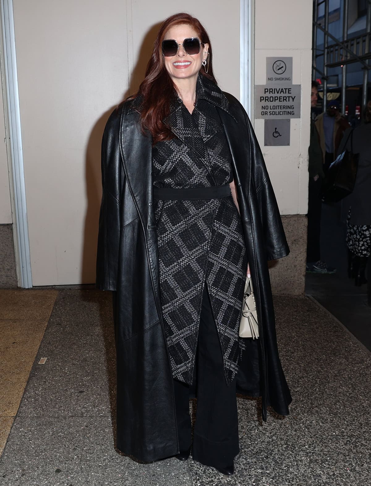 Debra Messing exudes power and confidence in a black and gray woven plaid wrap dress with wide-leg pants and a black leather coat