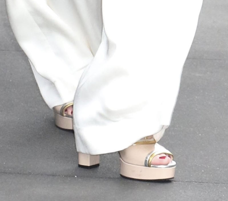 Debra Messing complements her white ensemble with nude beige open-toe sandals featuring silver and gold trims, platforms, and block heels